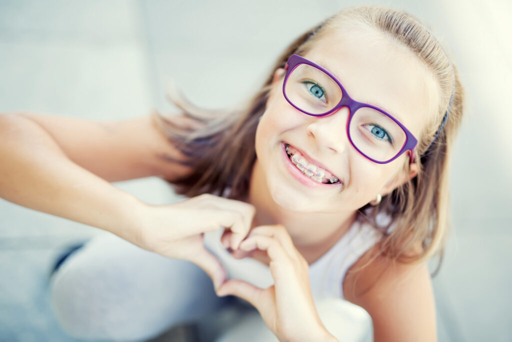 smiling little girl showing love heart symbol with hands.
